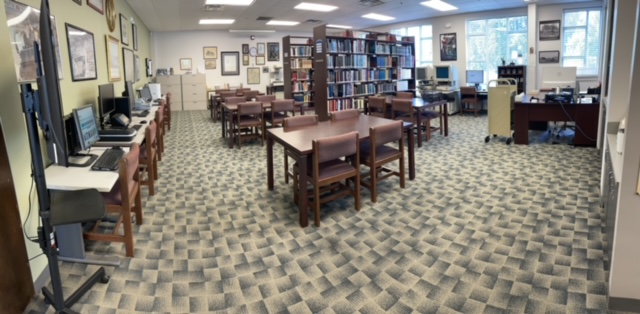 Interior Historical Research Center. Multiple tables with chairs, some free and a row by the wall with archiving tools. Bookshelves in the back.