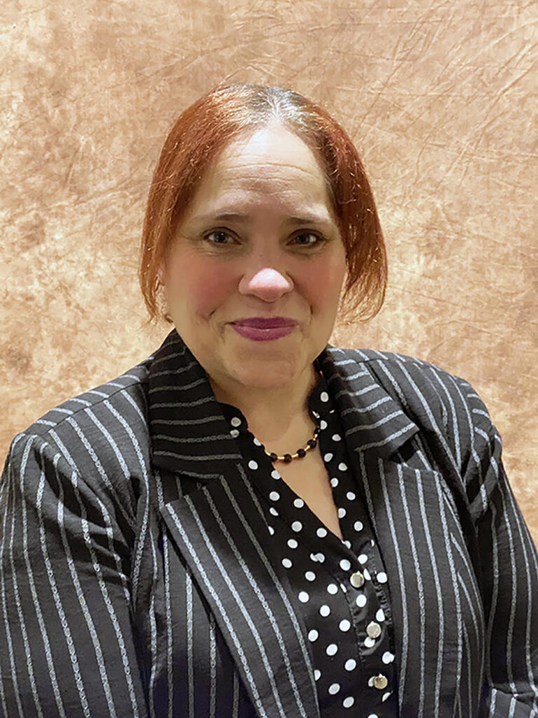 Latina woman with dyed red hair wearing a polka dot blouse and striped suit jacket