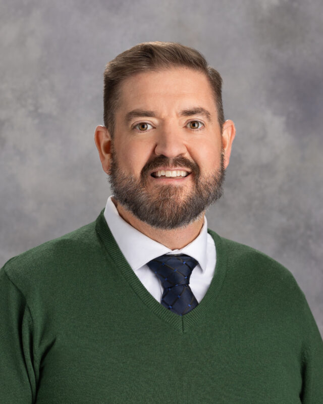 White man with brown hair and graying beard wearing a green sweater over 