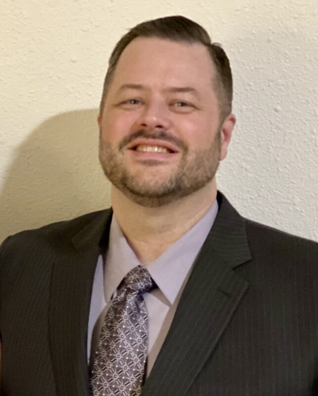 David Coutcher. White male. Brown hair. Wearing suit jacket, button up shirt and tie.